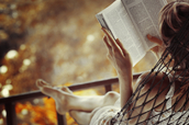 A woman reading a book on a hammock.
