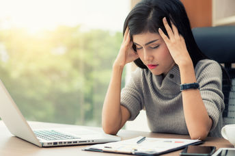 A young woman sits at her desk with a headache