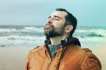 A man on the beach doing deep breathing exercises.