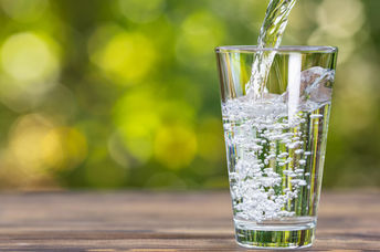 Drinking water from jug pouring into glass on wooden table outdoors