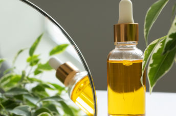 A bottle of vitamin E oil, nourishing for skin and hair, is beside a makeup mirror.