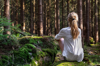 Woman sitting in green forest enjoys the silence and beauty of nature