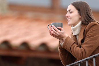 Happy woman contemplating the view and drinking coffee on a balcony in winter