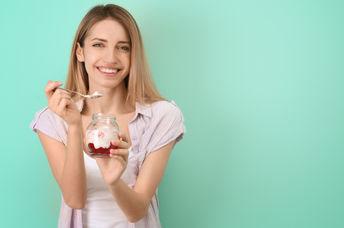 A young woman is eating a gut-healthy breakfast of yogurt with fruit.