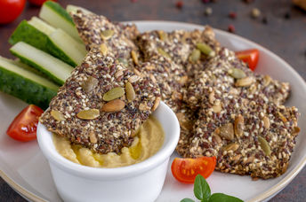 Homemade seed crackers are served with hummus and fresh vegetables.