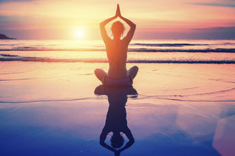 A woman meditates on the beach at sunset.
