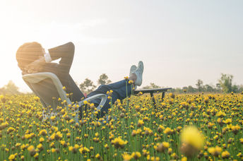 Businessman sitting in an office armchair and relaxing in a yellow flower field.