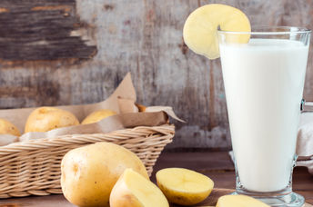 A glass of healthy potato milk is placed beside sustainable potatoes.