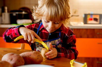 A little kid is carefully peeling potatoes in her kitchen.