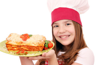 A smiling young girl is holding a plate of lasagna.