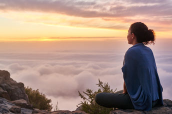 Woman sitting on a mountain top peacefully gazing at clouds