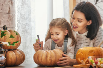 A mother carves a pumpkin for Halloween with her young daughter.