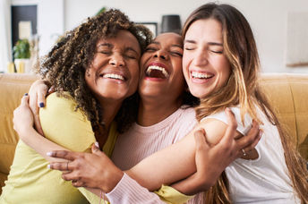 Three smiling friends enjoy a hug.