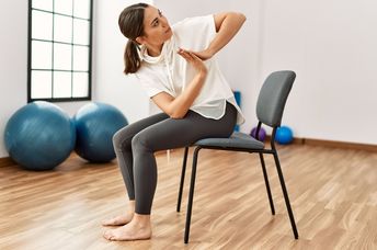 Woman performing chair yoga at a fitness center.