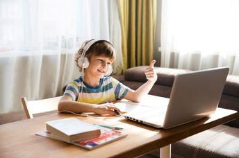 A boy wearing headphones gives a thumbs-up while using his laptop.