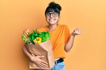 A woman smiles and holds a bag filled with food.