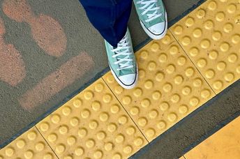 A woman walking on a yellow blind path for partially-sighted pedestrians.