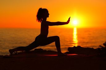 A woman does Tai Chi at sunset on the beach.