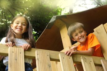 Smiling children look out from a wooden treehouse.