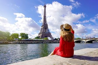 A woman sits on the quay of the Seine River looking at the Paris landmark Eiffel Tower.