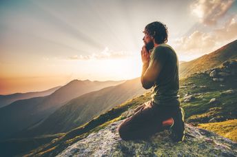 A man sits at sunset in the mountains.