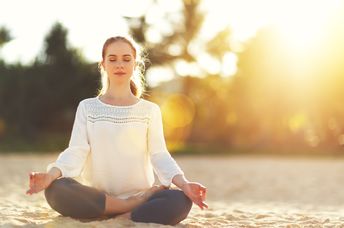 A woman practices yoga and meditates on the beach.