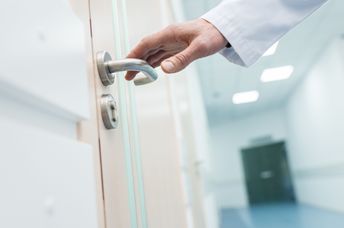 A doctor reaches for a door handle.
