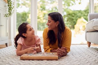 A mother and daughter lie on the floor at home.