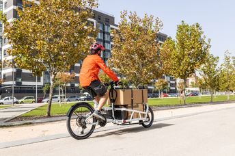 A young courier with a helmet rides a cargo bike.