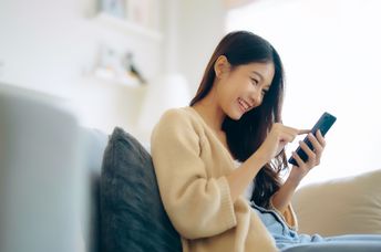 A woman sits on the couch using her phone.
