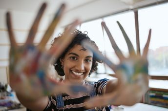 A woman smiles with colorful painted hands.