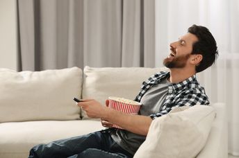 A man laughs while watching TV.