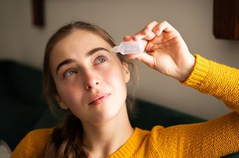 A woman using eye drops in a living room.