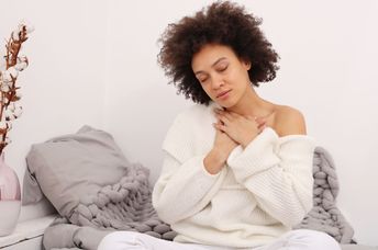 A woman sits with her hands on her chest.