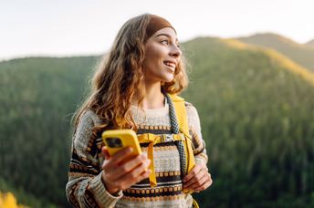 A woman walks in nature while holding her phone.