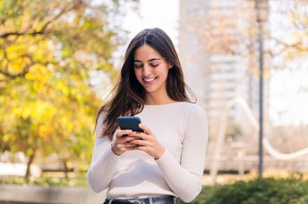 A woman smiles while she uses her phone.