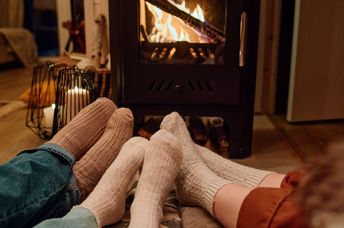 Three people wearing cozy socks sit together on the floor in front of a fireplace in a home.