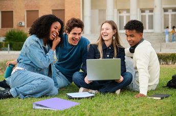 A diverse group of young adults sitting on the grass and smiling.