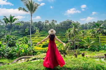 A female tourist in a red dress looks at a rice terrace in Bali, Indonesia.