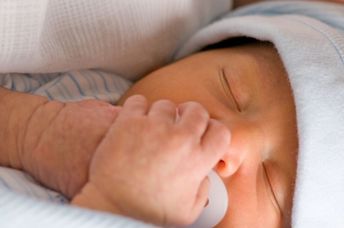 Newborn preemie holds his white pacifier.