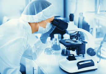 Young woman medical researcher looking through microscop slide in the life science