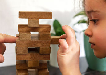 As a father and daughter play tumble tower, dad models resilience by assisting her in strengthening the tower.