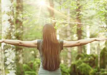 A woman in a forest spreads her arms out wide, showing balance and harmony.