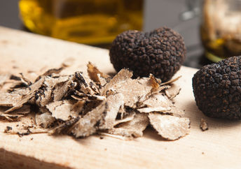 Black truffles and shaved truffles on a wooden cutting board.