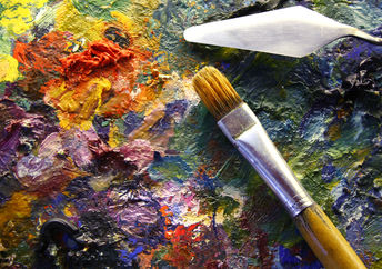 An artist’s palette with colorful paints, palette-knife, and brushes.