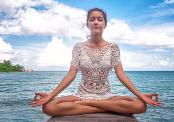 A woman meditates on a dock by a lake.