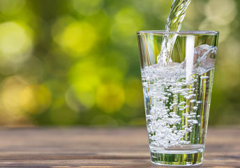 Drinking water from jug pouring into glass on wooden table outdoors