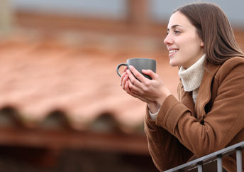 Happy woman contemplating the view and drinking coffee on a balcony in winter