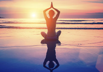 A woman meditates on the beach at sunset.