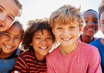 Close up of pre-teen friends in a park smiling to camera.